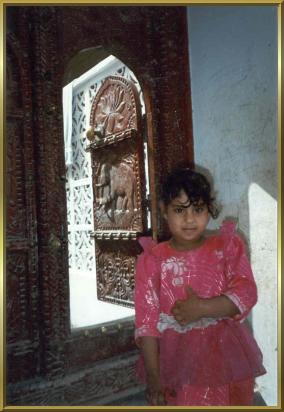 Ein Mädchen vor der kunstvoll geschnitzten Haustür in Sur